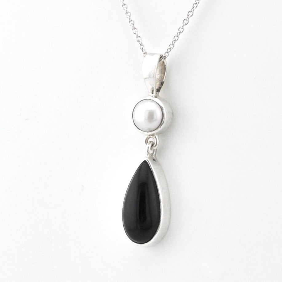 A silver pendant necklace featuring a round white pearl and a teardrop-shaped black onyx stone, suspended from a delicate silver chain against a plain white background.