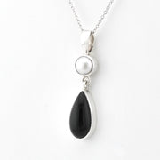A silver pendant necklace featuring a round white pearl and a teardrop-shaped black onyx stone, suspended from a delicate silver chain against a plain white background.