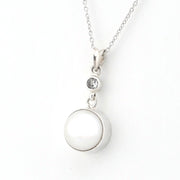 A silver pendant necklace featuring a large, smooth white oval pearl and a small clear round gemstone, shown on a delicate silver chain against a plain white background.