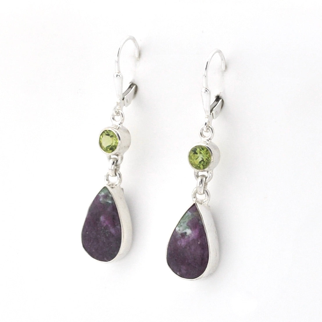 A pair of silver drop earrings featuring a small round green gemstone and a larger teardrop-shaped dark purple stone, shown on a plain white background.