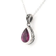 A silver teardrop pendant necklace featuring a faceted dark pinkish-red gemstone, set in an ornate silver bezel with a delicate silver chain against a white background.