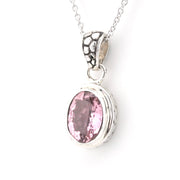 A silver pendant necklace featuring an oval-cut pink gemstone in a textured bezel setting, suspended from a delicate silver chain against a plain white background.