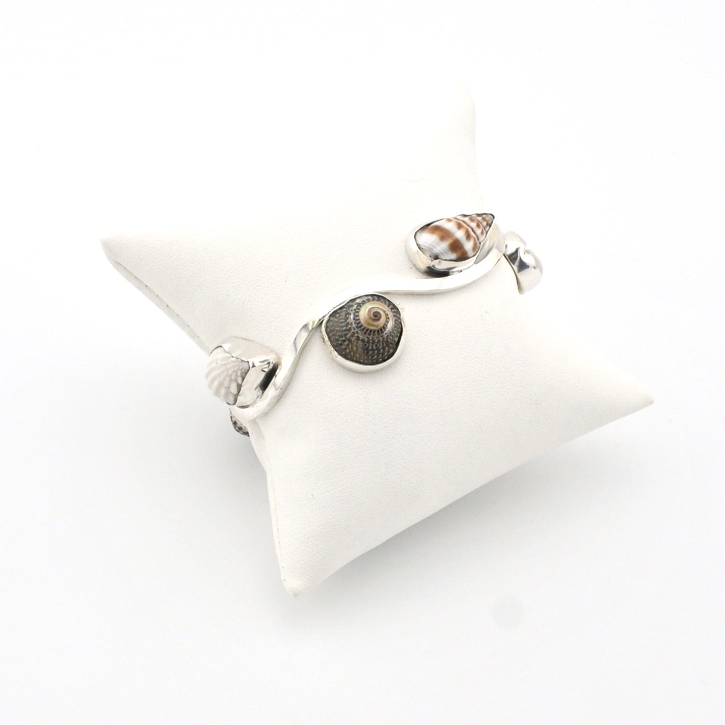 Silver shell bracelet on a white cushion against a white background