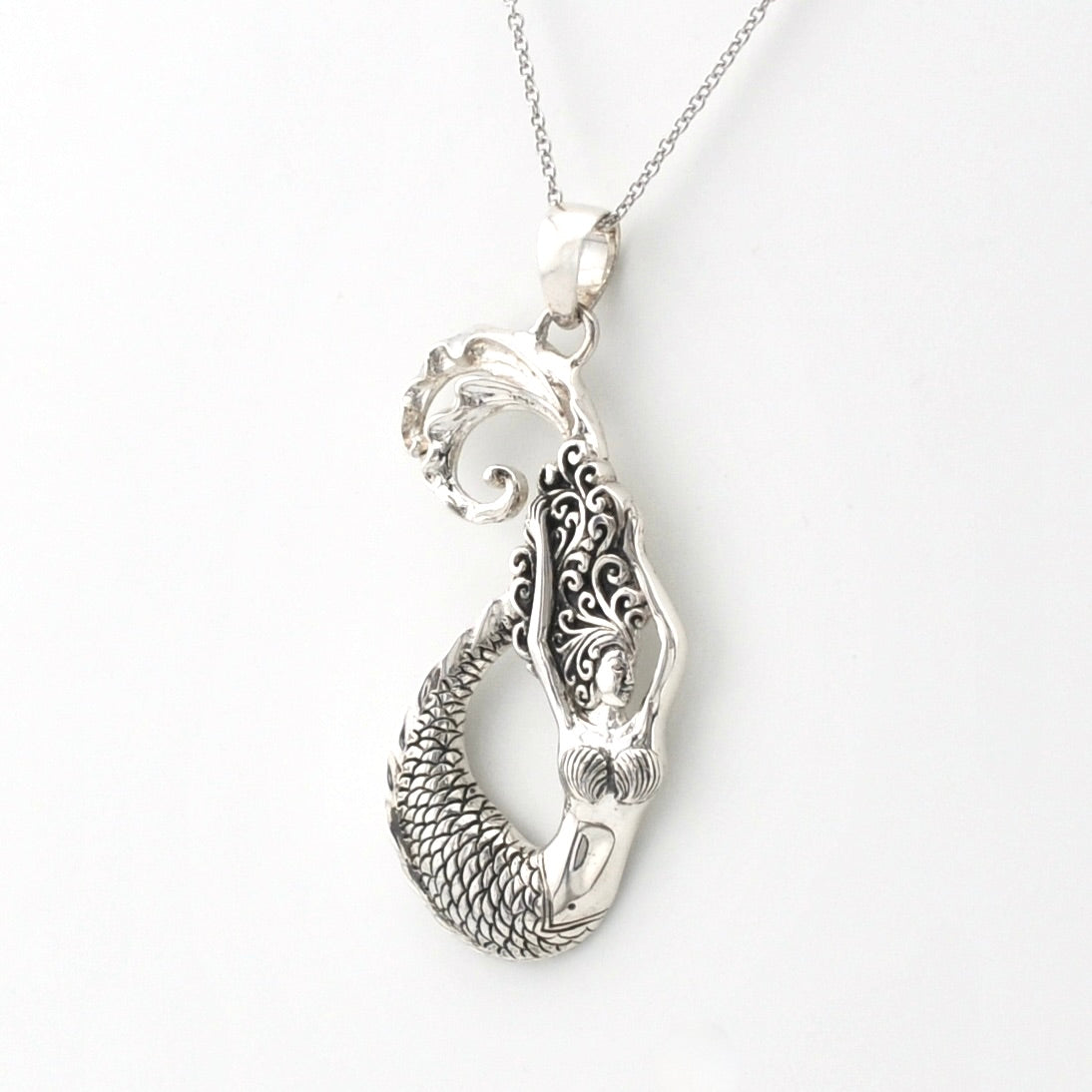 A sterling silver pendant necklace featuring a mermaid design with detailed scrollwork and a textured scale tail, shown on a clean white background.