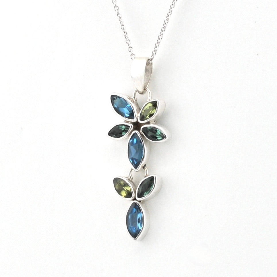 A silver pendant necklace featuring a floral design with marquise-cut blue and olive green gemstones, shown against a plain white background.