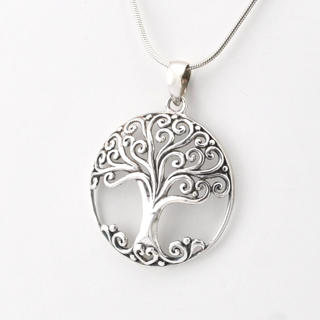 A silver tree of life pendant necklace with an intricate scrollwork design, hanging from a silver snake chain against a plain white background.