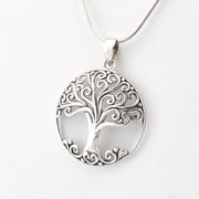 A silver tree of life pendant necklace with an intricate scrollwork design, hanging from a silver snake chain against a plain white background.