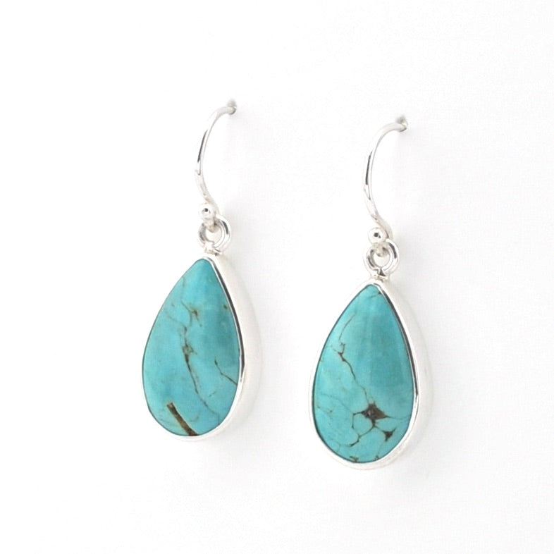 A pair of silver drop earrings featuring teardrop-shaped turquoise stones with natural dark matrix veining, set in polished silver bezels with silver French hook ear wires, shown on a plain white background.