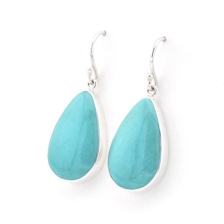 A pair of silver drop earrings featuring teardrop-shaped turquoise stones in polished silver bezel settings, shown against a plain white background.