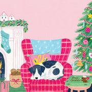 A cozy Christmas illustration featuring a black and white dog sleeping on a pink plaid armchair with a blue starry pillow. A pink Christmas tree stands on the right, a fireplace with a green stocking and mantel is on the left, and a small gift box labeled 'Hand Chocolates' sits on a table in the foreground against a soft pink background.