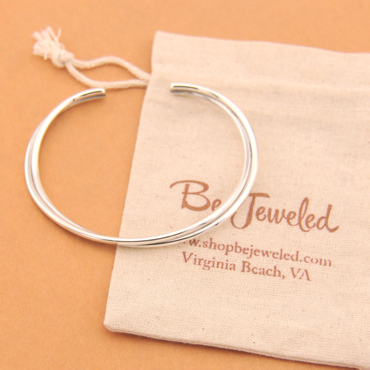 Silver bracelet on a Be Jeweled branded pouch against a beige background