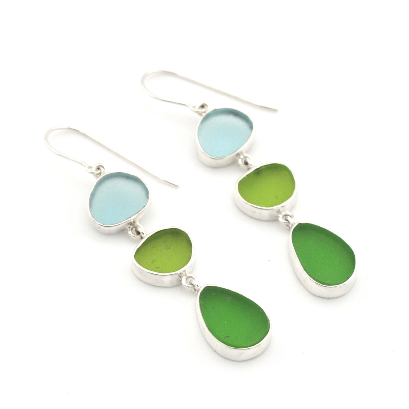 A pair of silver drop earrings featuring three stacked, organic-shaped sea glass pieces in light blue, olive green, and medium green, set against a plain white background.