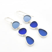 A pair of silver drop earrings featuring three teardrop-shaped blue glass stones of varying shades, displayed on a clean white background.
