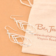 Silver earrings on a beige surface with a branded bag in the background