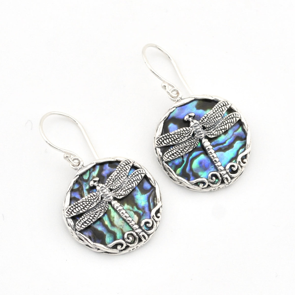 A pair of silver dragonfly drop earrings featuring oval abalone shell inlays with iridescent blue, green, and purple hues, set against a plain white background.