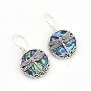 A pair of silver dragonfly drop earrings featuring oval abalone shell inlays with iridescent blue, green, and purple hues, set against a plain white background.