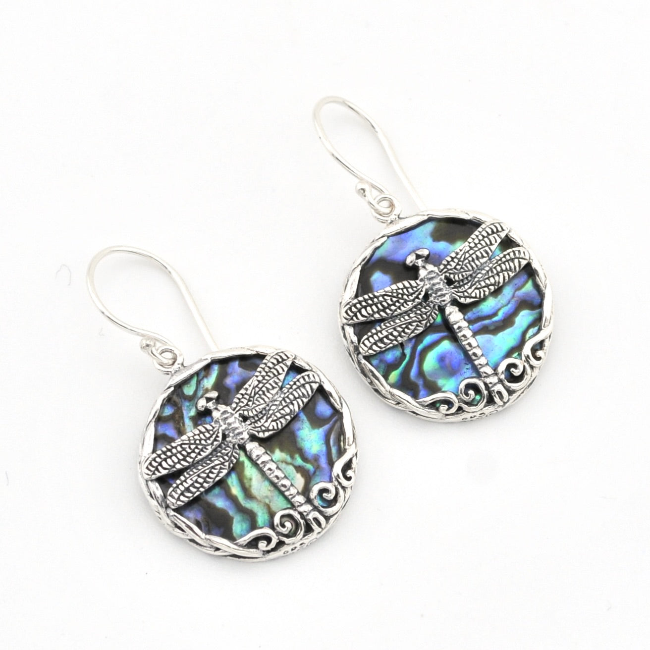 A pair of silver dragonfly drop earrings featuring oval abalone shell inlays with iridescent blue, green, and purple hues, set against a plain white background.
