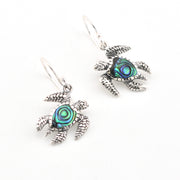 Silver turtle earrings with abalone shell centers on a white background