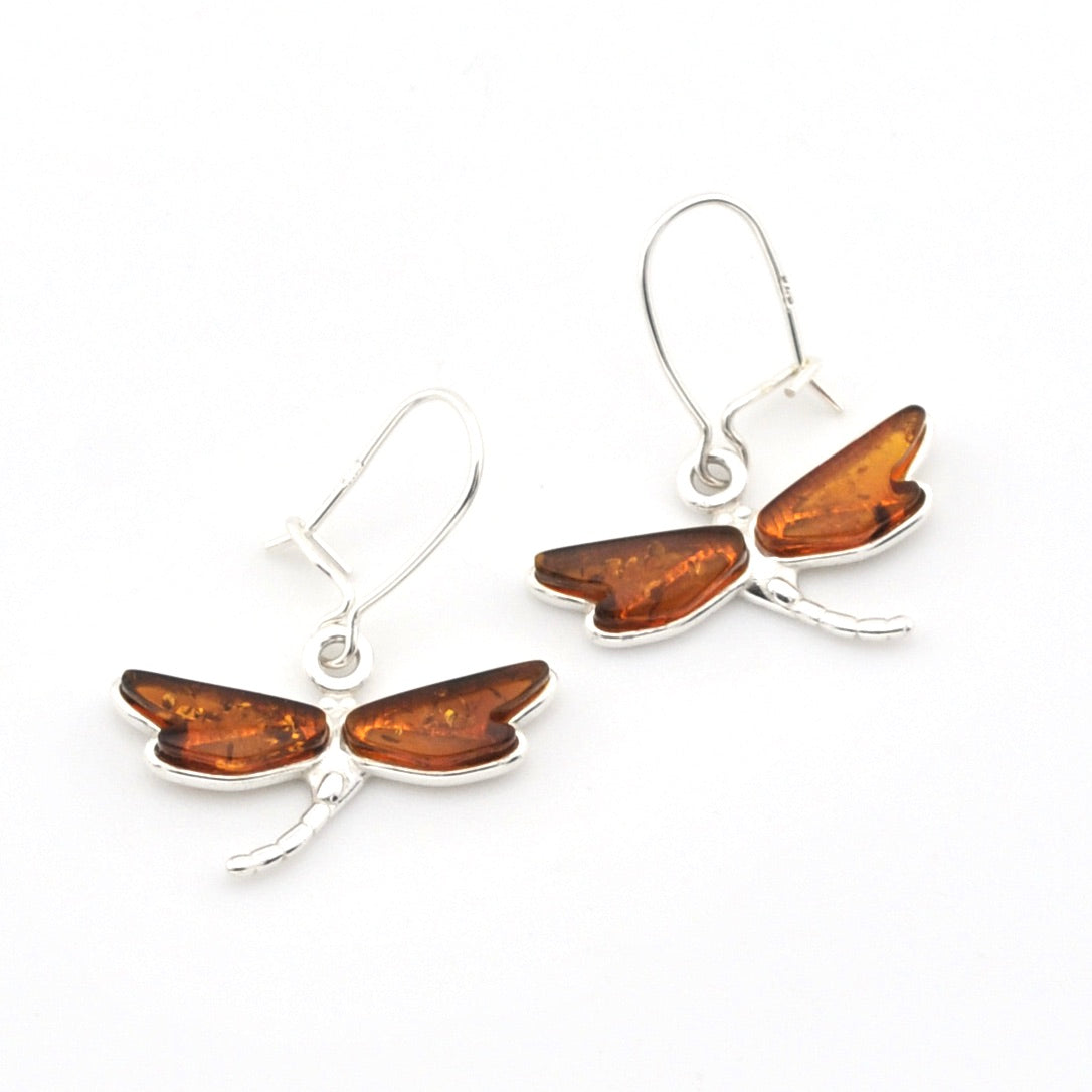 A pair of silver fishhook earrings featuring a dragonfly awith mber wings and a small silver body, displayed on a clean white background.