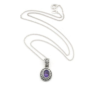 An oval pendant necklace featuring a purple amethyst stone set in a silver-toned, ornate filigree bezel on a delicate silver chain, displayed against a solid white background.