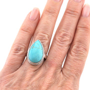 A close-up of a hand wearing a silver ring with a large teardrop-shaped turquoise stone.