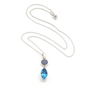 A silver necklace featuring a marquise-cut blue topaz pendant and a small oval opal stone, displayed on a clean white background.