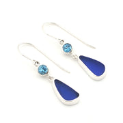 A pair of silver drop earrings featuring a small round light blue topaz and a larger teardrop-shaped dark blue sea glass, shown on a plain white background.