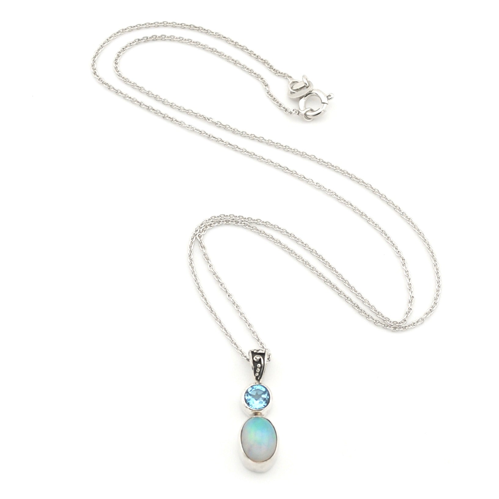 A silver necklace featuring a pendant with a small round light blue gemstone and an oval iridescent opal stone, displayed on a clean white background.