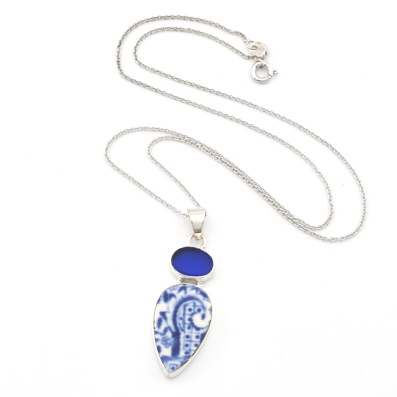 Silver necklace with a teardrop-shaped blue and white patterned porcelain pendant and a small round blue stone above it, shown on a white background.