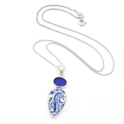 Silver necklace with a teardrop-shaped blue and white patterned porcelain pendant and a small round blue stone above it, shown on a white background.
