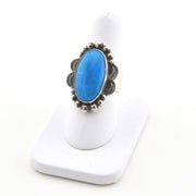 Blue stone ring with silver decorative band on a white stand
