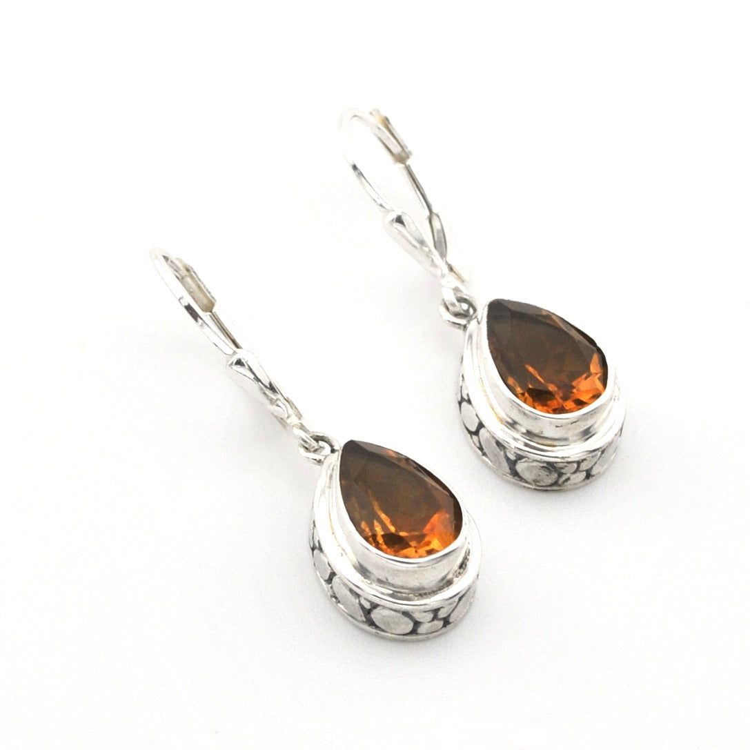 A pair of silver leverback drop earrings featuring teardrop-shaped orange gemstones in a textured silver bezel setting, shown on a plain white background.