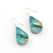 A pair of teardrop-shaped dangle earrings with iridescent blue, green, and gold dichroic glass set in silver, hanging from silver fishhook wires on a plain white background.