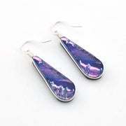 A pair of teardrop-shaped dangle earrings with silver fishhook wires and iridescent purple, blue, and pink glass inlays, displayed on a clean white background.