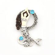 Decorative pendant with intricate designs and blue gemstones on a white background