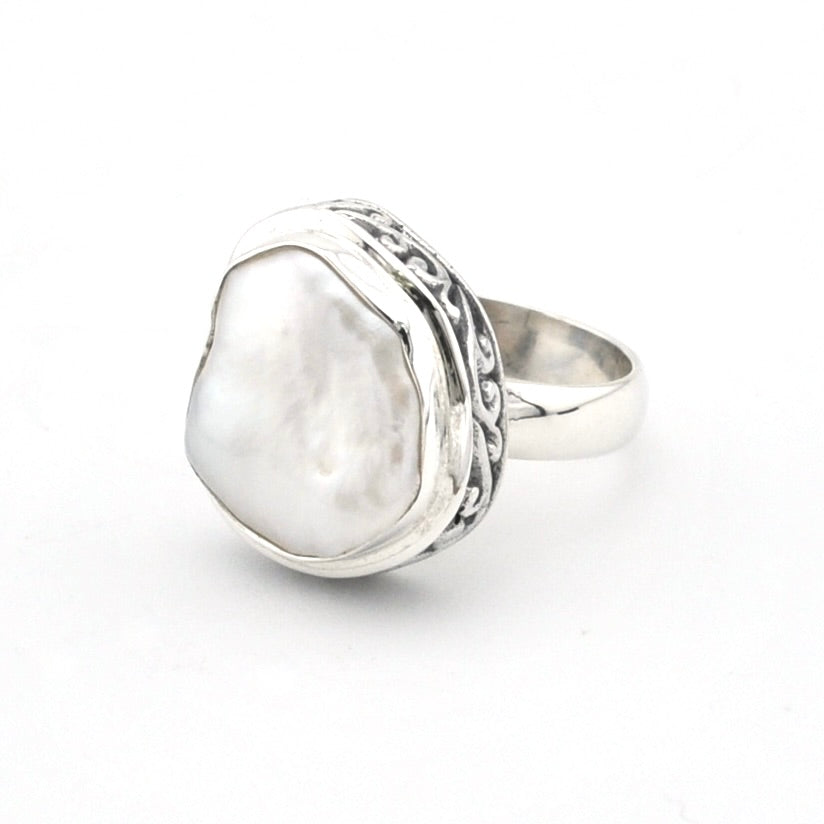 A sterling silver ring featuring a large, organic-shaped white pearl bezel-set in an ornate, textured frame, shown on a plain white background.