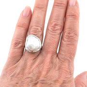 A close-up of a hand wearing a large silver ring with an irregular, organic-shaped white stone.