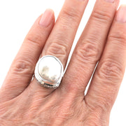 A silver ring with a large, irregularly shaped polished white stone, shown worn on a person's finger against a plain white background.