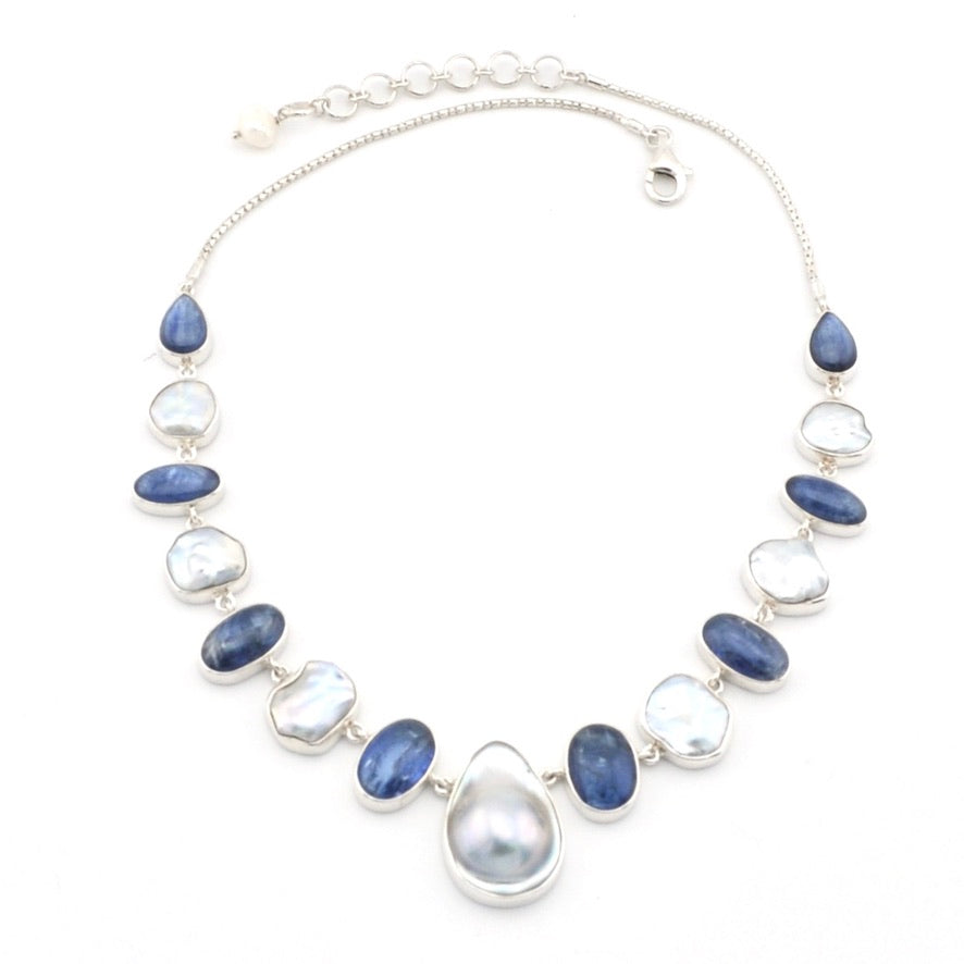 A silver necklace featuring a central teardrop-shaped gray pearl surrounded by alternating smooth oval blue kyanite and irregular keshi white pearls, set in silver bezels on a white background.