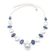A silver necklace featuring a central teardrop-shaped gray pearl surrounded by alternating smooth oval blue kyanite and irregular keshi white pearls, set in silver bezels on a white background.