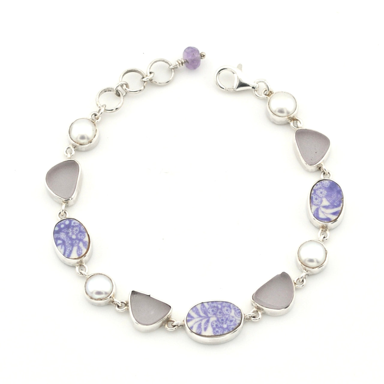 A silver link bracelet featuring alternating round white pearls, smooth light gray teardrop-shaped stones, and oval and marquise-cut lavender and white porcelain, shown on a plain white background.