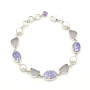 A silver link bracelet featuring alternating round white pearls, smooth light gray teardrop-shaped stones, and oval and marquise-cut lavender and white porcelain, shown on a plain white background.