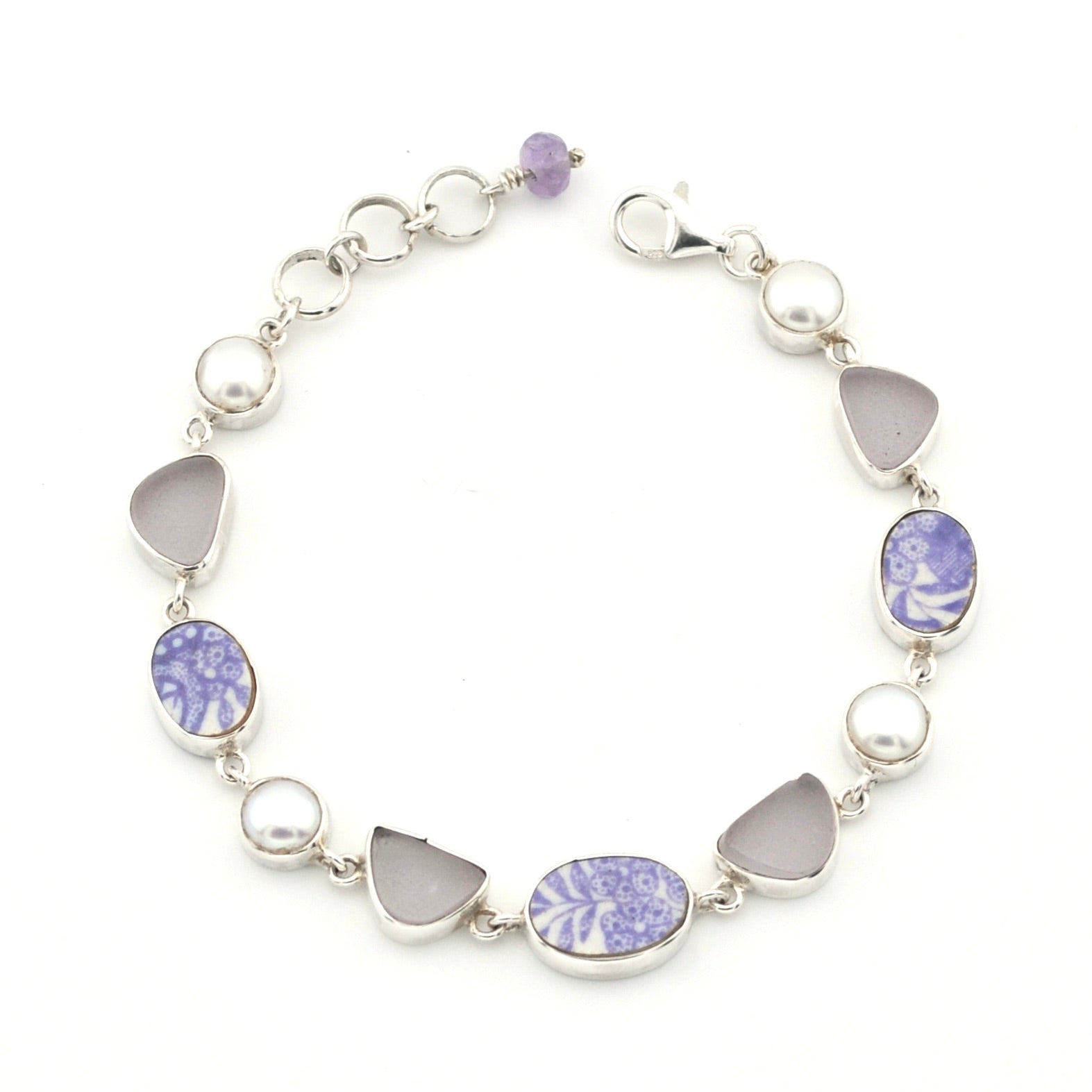 A silver link bracelet featuring alternating round white pearls, smooth light gray teardrop-shaped stones, and oval and marquise-cut lavender and white porcelain, shown on a plain white background.