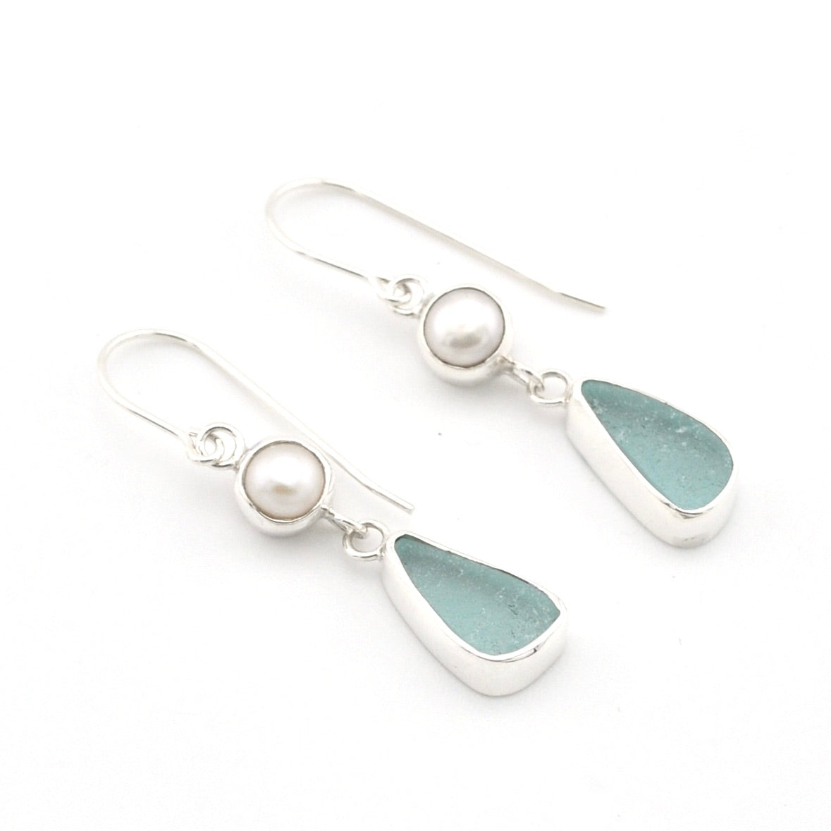 A pair of silver drop earrings featuring a small white pearl and a teardrop-shaped light blue-green sea glass stone, shown on a clean white background.