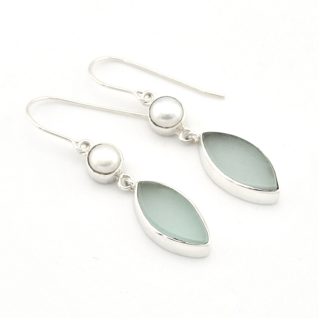 A pair of silver dangle earrings featuring oval milky white pearl beads and teardrop-shaped light green sea glass stones, set against a plain white background.