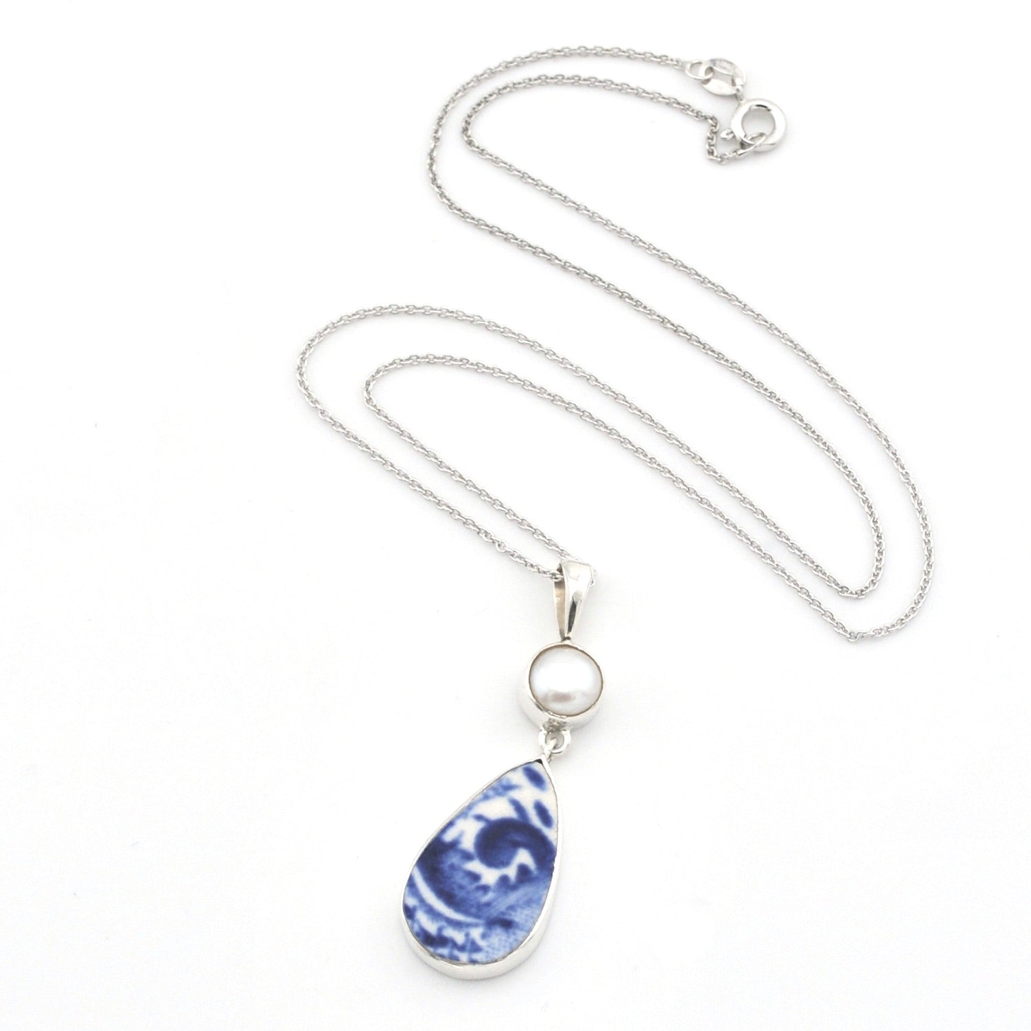A silver chain necklace featuring a teardrop-shaped pendant with a blue and white marbled pattern, accented by a small round white pearl, shown on a plain white background.