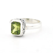 A sterling silver ring featuring a rectangular green peridot gemstone in a decorative bezel setting, shown on a plain white background.