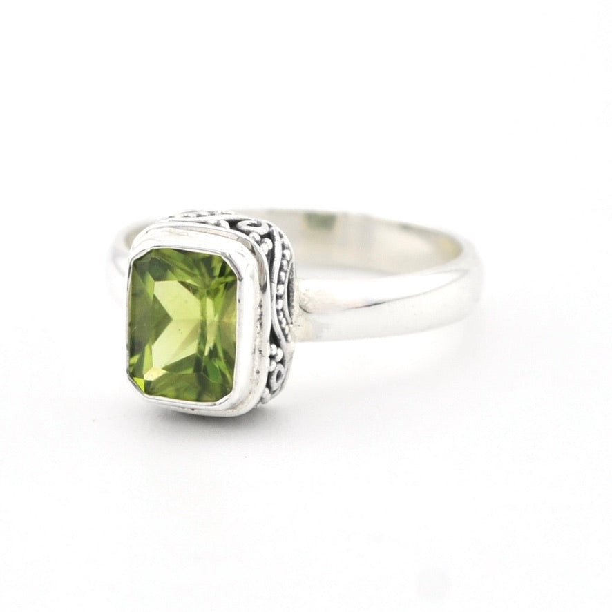 A sterling silver ring featuring a rectangular green peridot gemstone in a decorative bezel setting, shown on a plain white background.