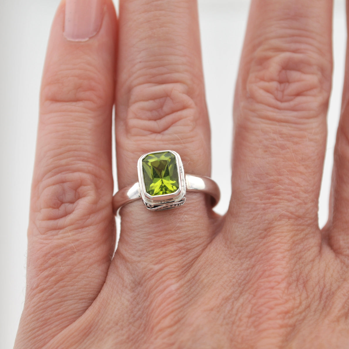 A sterling silver ring with a rectangular green peridot gemstone, shown worn on a person's finger against a plain white background.