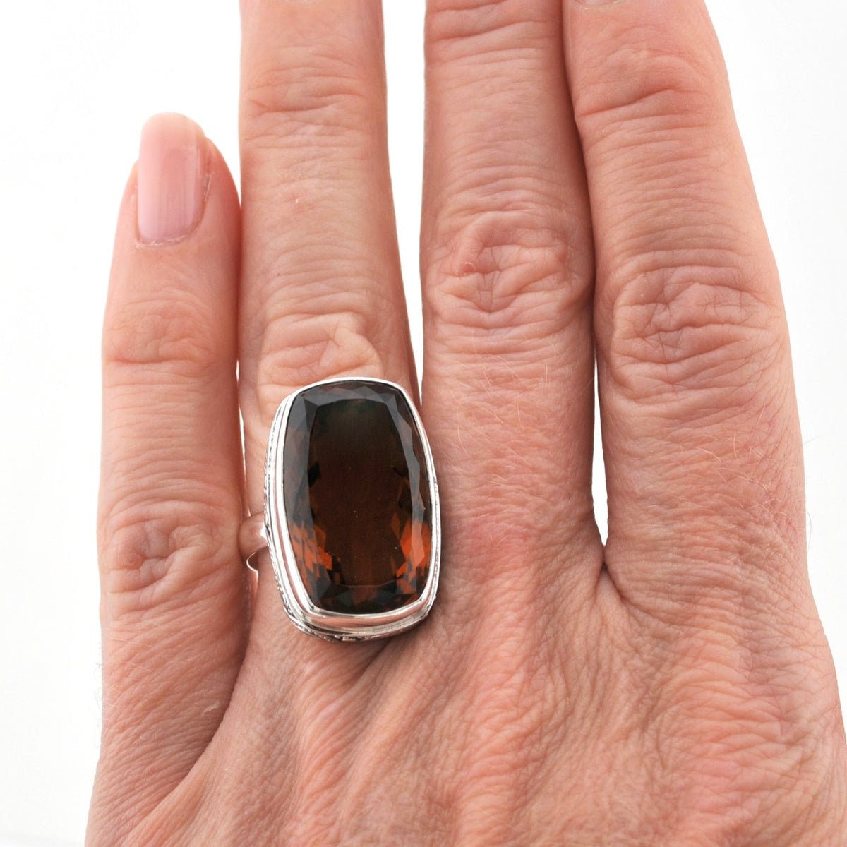 A silver ring with a large, cushion-cut dark brown gemstone, shown worn on a person's finger against a plain white background.